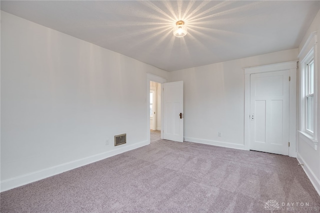 spare room featuring baseboards, visible vents, and light colored carpet