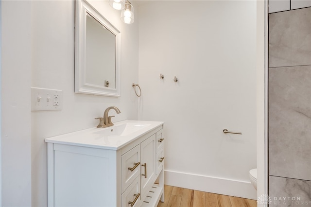 bathroom with toilet, wood finished floors, vanity, and baseboards