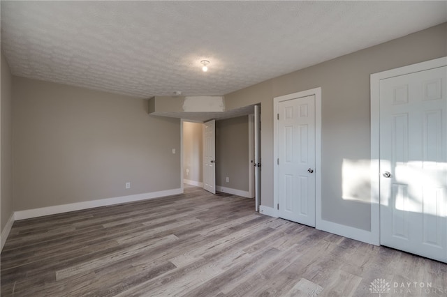 unfurnished bedroom featuring a textured ceiling, baseboards, and wood finished floors