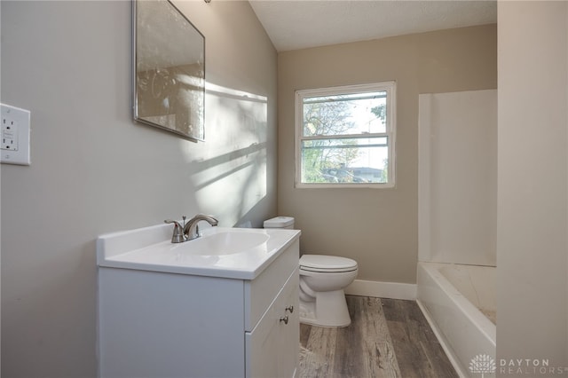 full bathroom with baseboards, toilet, wood finished floors, vanity, and a bath