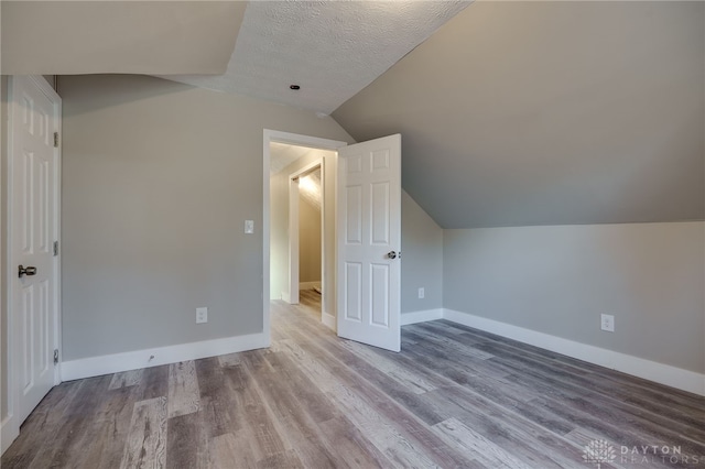 additional living space featuring a textured ceiling, baseboards, vaulted ceiling, and wood finished floors