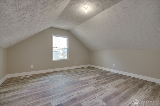 bonus room with lofted ceiling, visible vents, a textured ceiling, wood finished floors, and baseboards