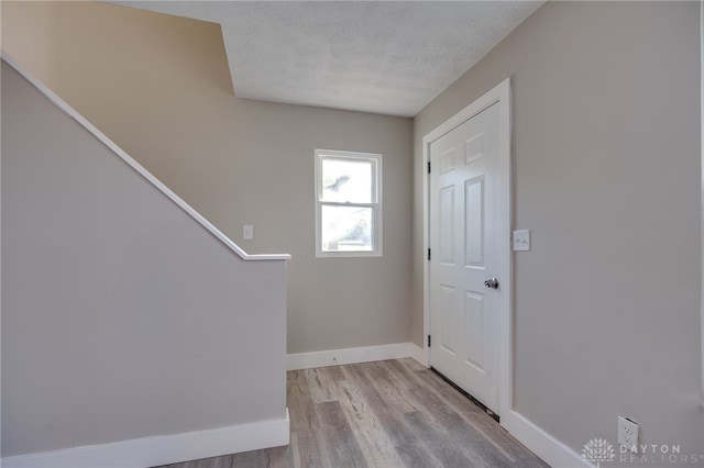 entryway with a textured ceiling, stairway, wood finished floors, and baseboards