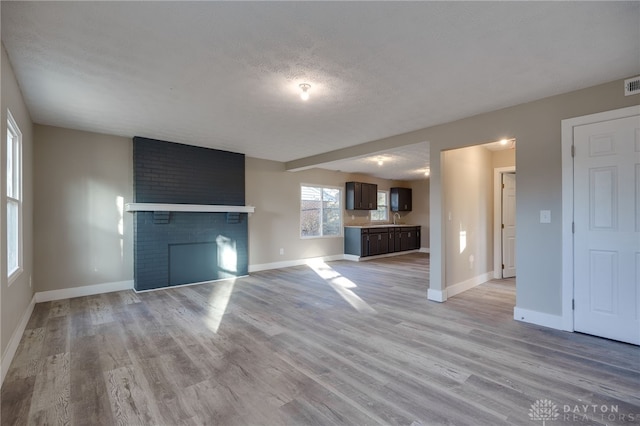 unfurnished living room featuring light wood finished floors, a fireplace, baseboards, and a textured ceiling