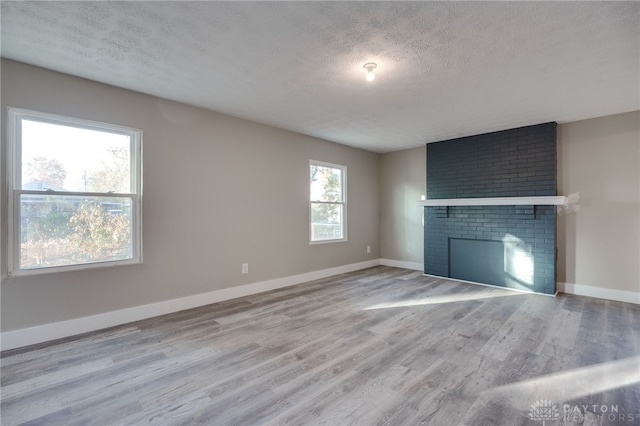 unfurnished living room with a fireplace, a textured ceiling, baseboards, and wood finished floors