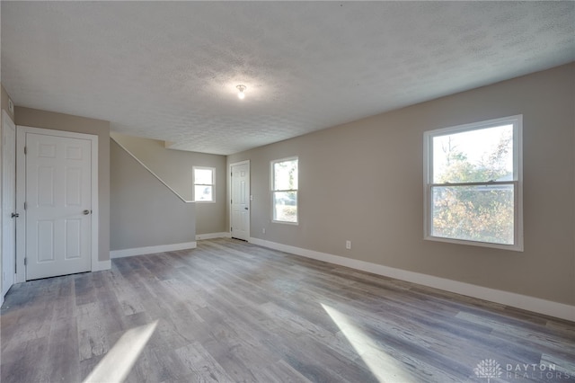 spare room with a textured ceiling, light wood finished floors, and baseboards