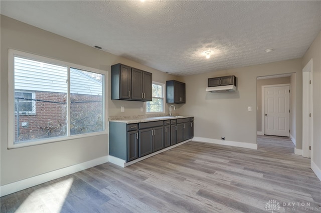 kitchen featuring light countertops, a sink, a textured ceiling, light wood-type flooring, and baseboards