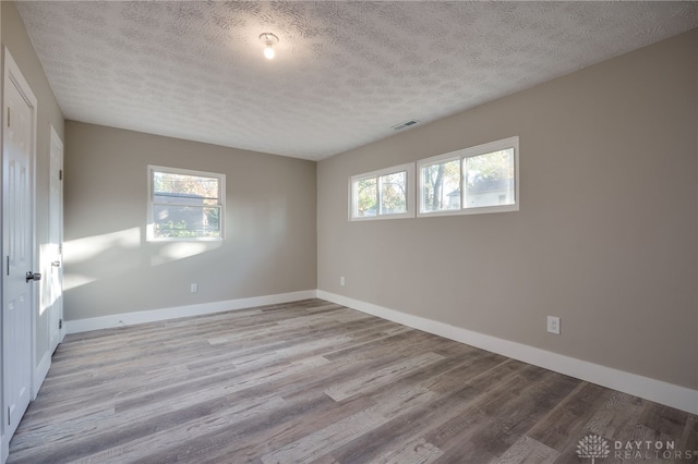 spare room featuring baseboards, a textured ceiling, visible vents, and wood finished floors