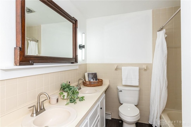 full bathroom with a wainscoted wall, double vanity, a sink, and tile walls