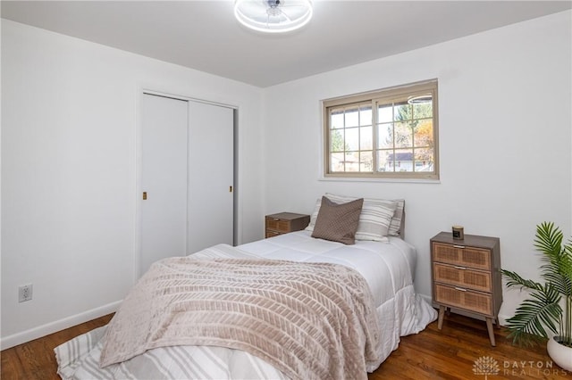 bedroom with dark wood-type flooring, a closet, and baseboards