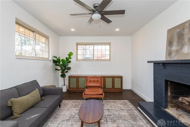 living room featuring dark wood-style floors, a wealth of natural light, a brick fireplace, and baseboards