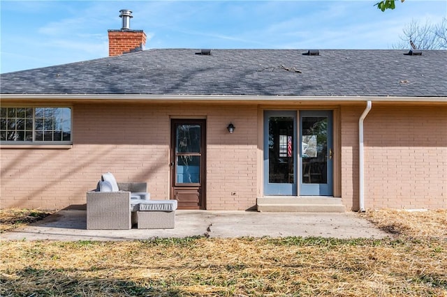 view of exterior entry featuring a patio, brick siding, and a shingled roof