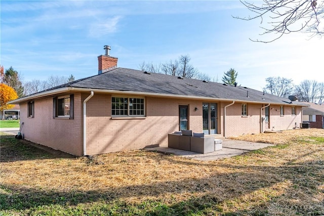 rear view of house with brick siding, a yard, a chimney, roof with shingles, and a patio area