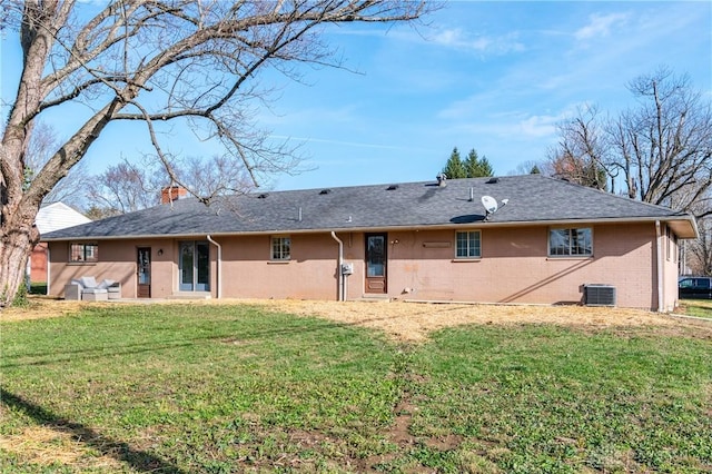 back of property with a chimney, central AC unit, a lawn, and brick siding