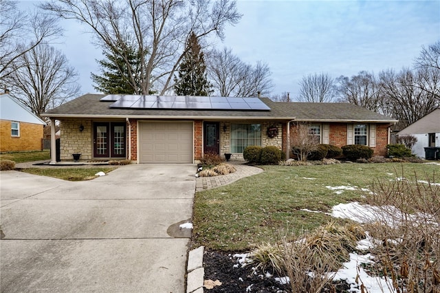 ranch-style home featuring a garage, concrete driveway, a front yard, and roof mounted solar panels