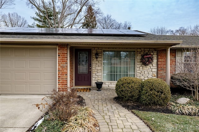 doorway to property with an attached garage, a shingled roof, roof mounted solar panels, and brick siding