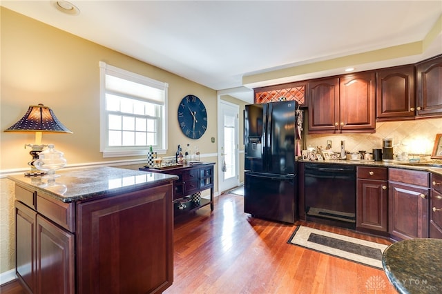 kitchen featuring backsplash, dark wood-style flooring, stone counters, black appliances, and a sink