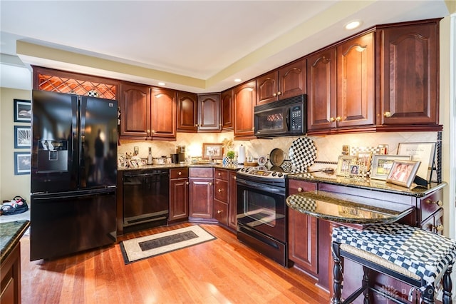 kitchen featuring light wood finished floors, tasteful backsplash, recessed lighting, dark stone counters, and black appliances