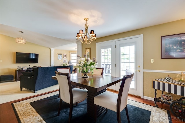 dining space featuring lofted ceiling, a notable chandelier, ornate columns, and wood finished floors