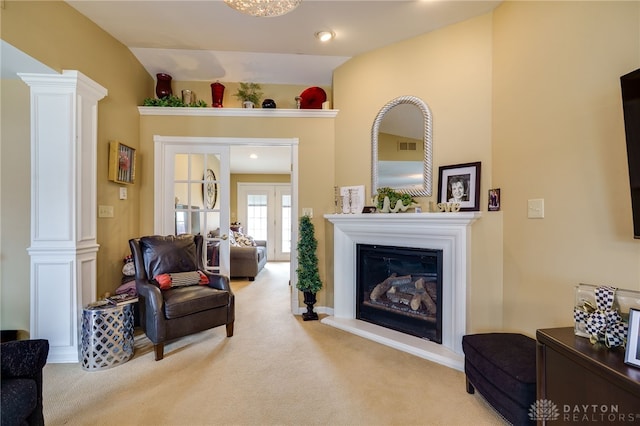 living room with light carpet, decorative columns, visible vents, a glass covered fireplace, and vaulted ceiling