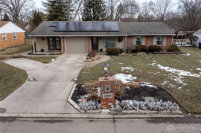 ranch-style house featuring solar panels, concrete driveway, an attached garage, a front lawn, and brick siding