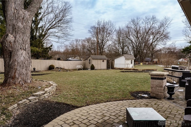 view of yard with a storage shed, a fenced backyard, a patio area, and an outbuilding