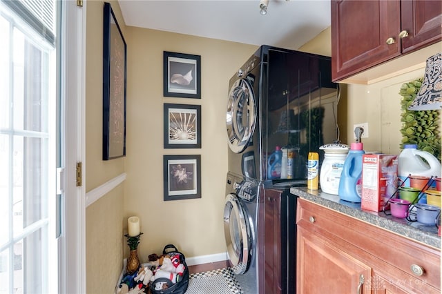 clothes washing area with stacked washer / drying machine, cabinet space, and baseboards