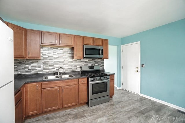 kitchen featuring stainless steel appliances, a sink, decorative backsplash, brown cabinetry, and dark countertops