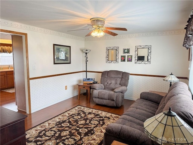 living area with a ceiling fan, wood finished floors, baseboards, and wallpapered walls