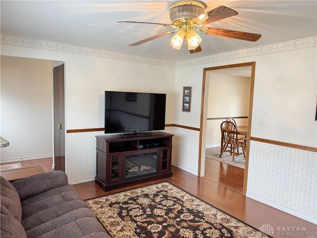 living area with a wainscoted wall, wood finished floors, a ceiling fan, and wallpapered walls