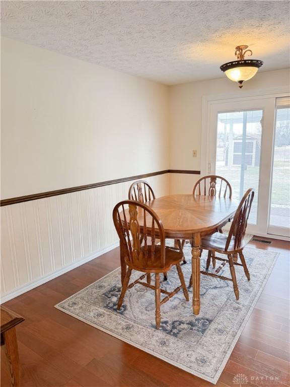 dining area featuring visible vents, a wainscoted wall, dark wood finished floors, and a textured ceiling