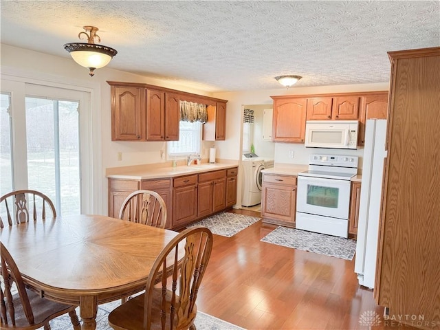 kitchen featuring white appliances, plenty of natural light, wood finished floors, light countertops, and a sink