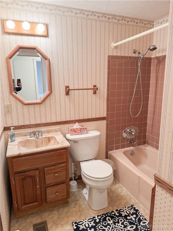 full bathroom with a textured ceiling, toilet, vanity, tub / shower combination, and wallpapered walls