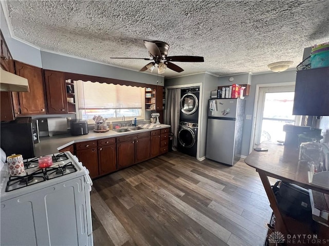 kitchen featuring white range with gas stovetop, freestanding refrigerator, light countertops, stacked washing maching and dryer, and a sink