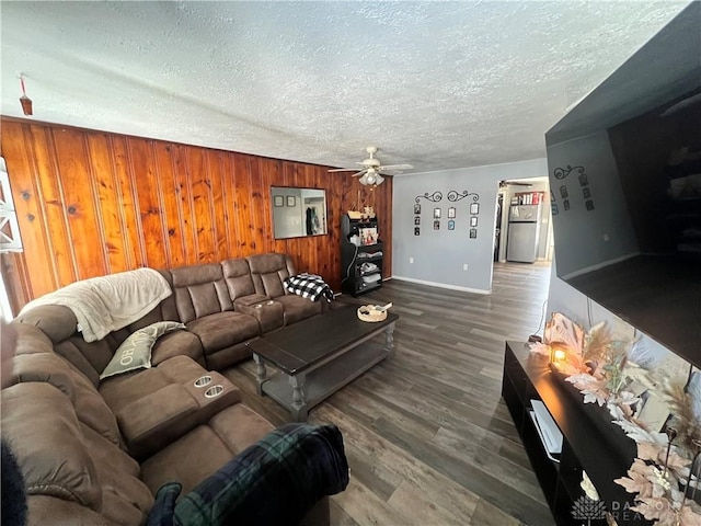 living area featuring dark wood-type flooring, wood walls, a textured ceiling, and a ceiling fan