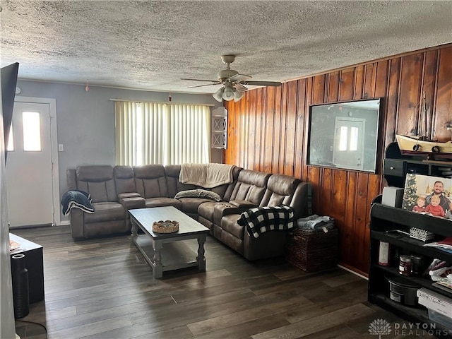 living area featuring a textured ceiling, ceiling fan, dark wood-type flooring, and wood walls