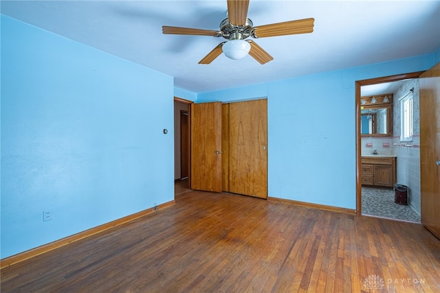 unfurnished bedroom with connected bathroom, a closet, baseboards, and dark wood-type flooring