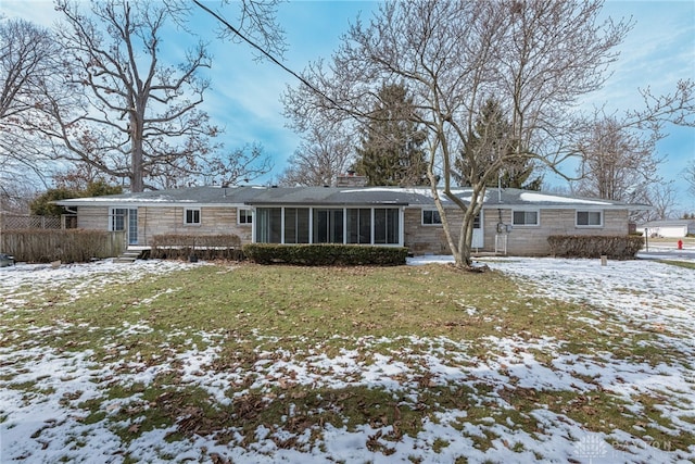 snow covered property featuring a sunroom, stone siding, a chimney, and a yard