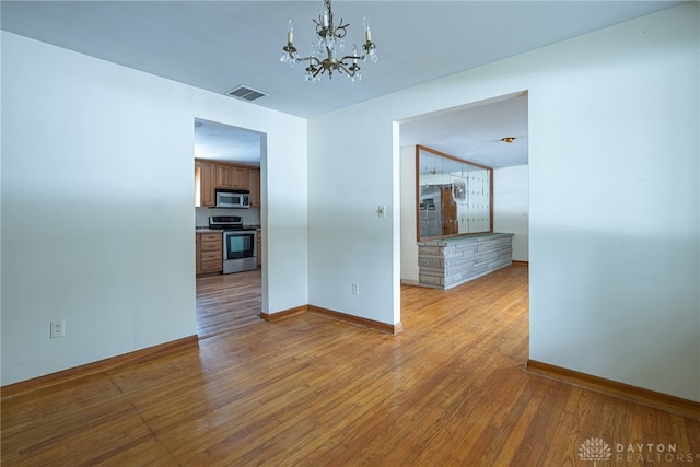 unfurnished room featuring light wood-style floors, a chandelier, visible vents, and baseboards