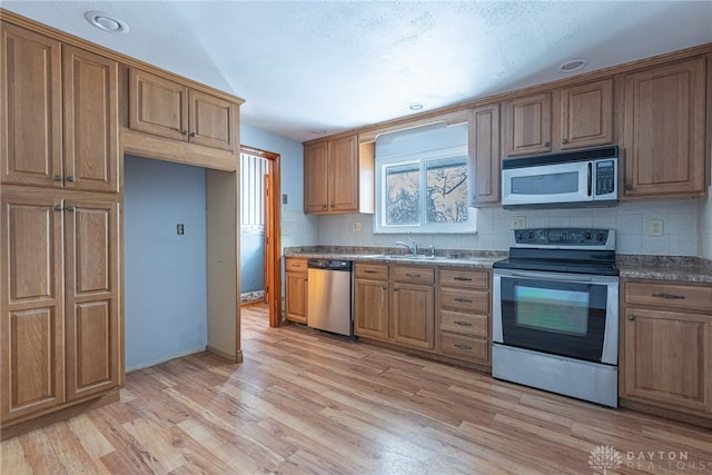 kitchen featuring brown cabinets, stainless steel appliances, dark countertops, tasteful backsplash, and light wood-type flooring