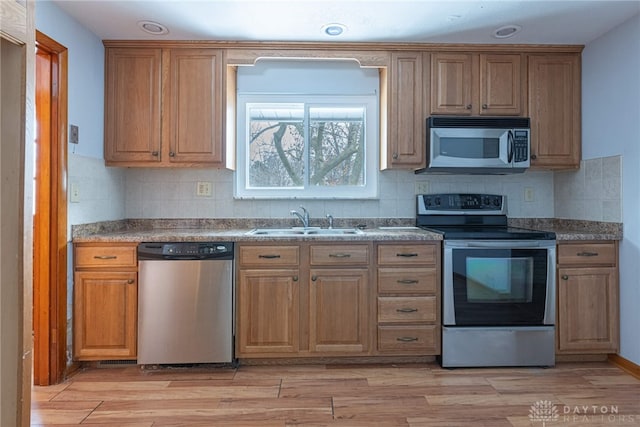 kitchen with stainless steel appliances, tasteful backsplash, a sink, and light wood-style flooring