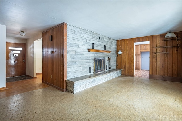 unfurnished living room with wooden walls, a fireplace, and baseboards