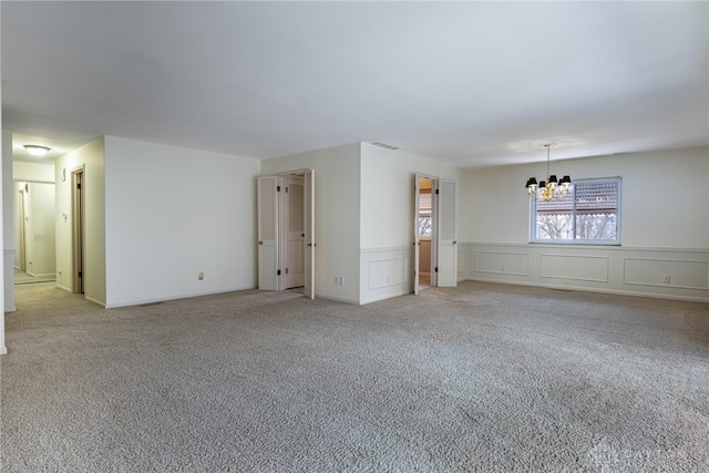 unfurnished room with a notable chandelier, a decorative wall, light colored carpet, visible vents, and wainscoting