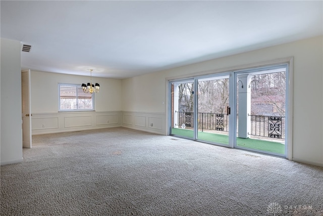 unfurnished room with carpet floors, visible vents, a decorative wall, and an inviting chandelier