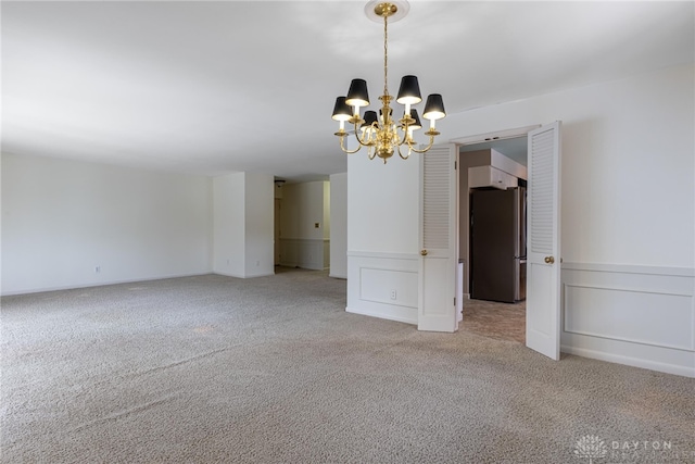 spare room featuring a notable chandelier, a decorative wall, and carpet flooring