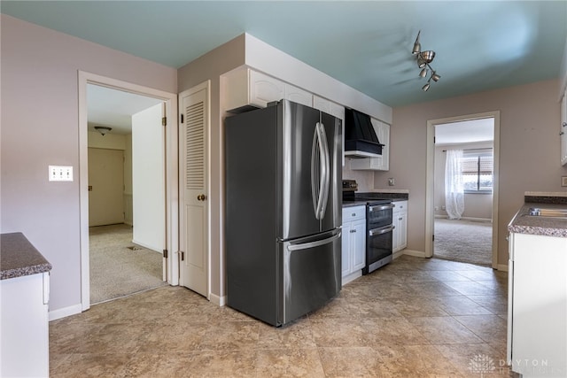 kitchen featuring dark countertops, custom range hood, appliances with stainless steel finishes, light carpet, and white cabinetry