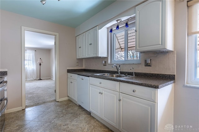 kitchen with white dishwasher, a sink, white cabinets, backsplash, and dark countertops