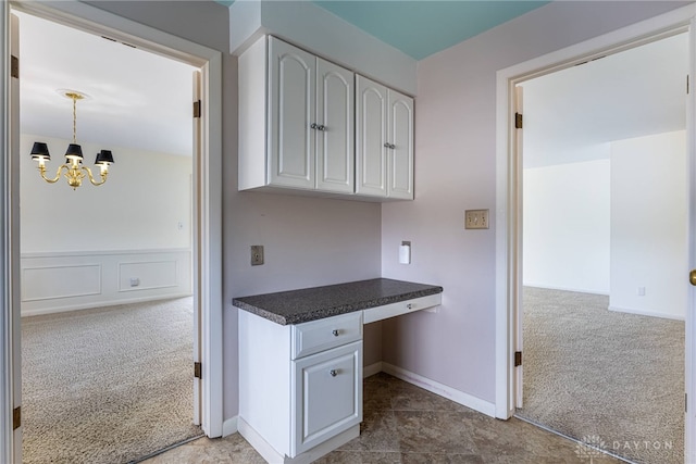 kitchen featuring built in desk, dark countertops, carpet floors, white cabinetry, and a notable chandelier