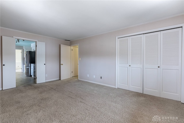 unfurnished bedroom featuring carpet floors, baseboards, ornamental molding, a closet, and freestanding refrigerator