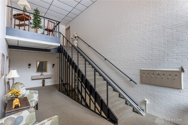 stairs with brick wall, a drop ceiling, mail area, and a high ceiling